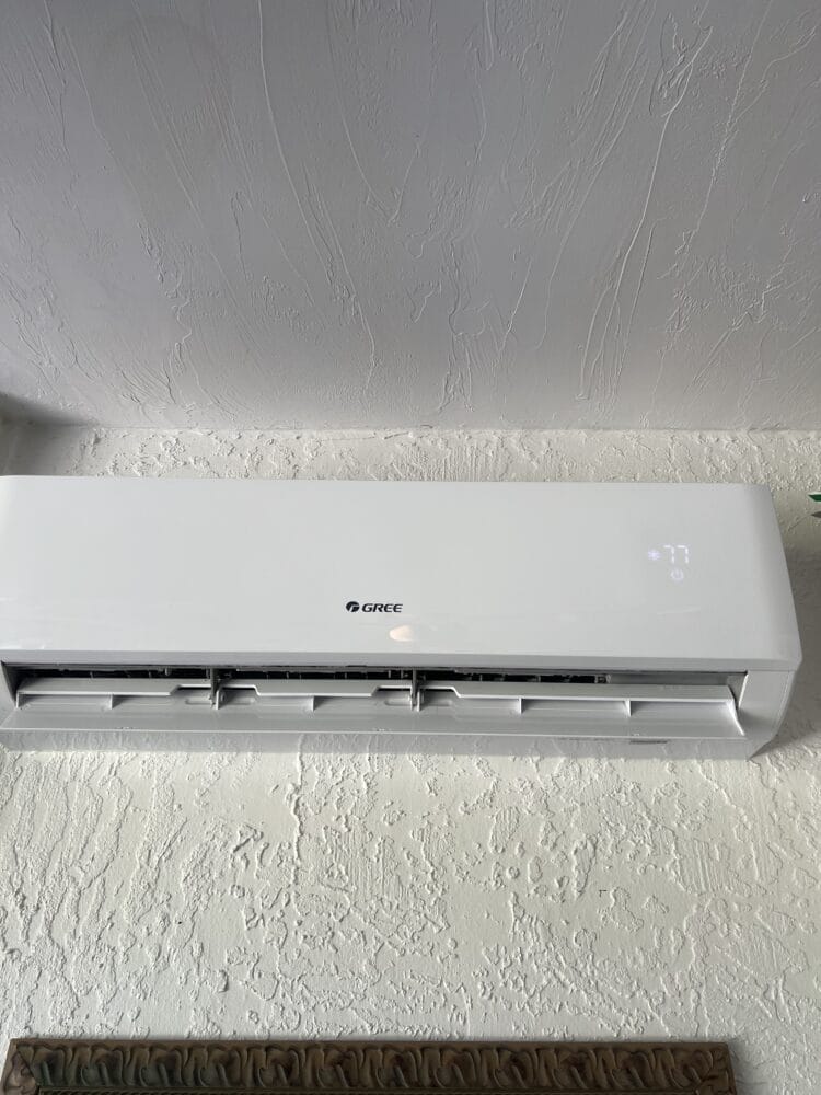 Wall-mounted Gree mini split air conditioning unit installed on a textured interior wall, displaying a digital temperature setting of 77 degrees.