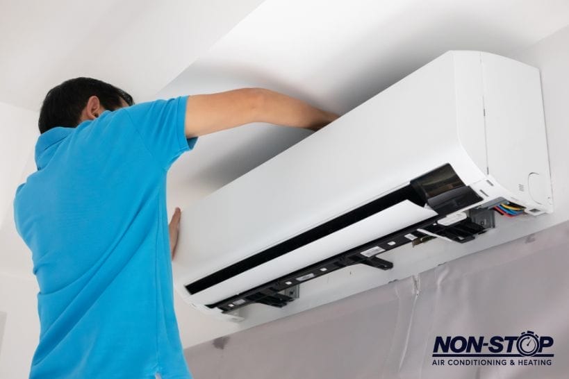 Technician servicing a wall-mounted ductless mini-split air conditioner during indoor HVAC maintenance or repair.
